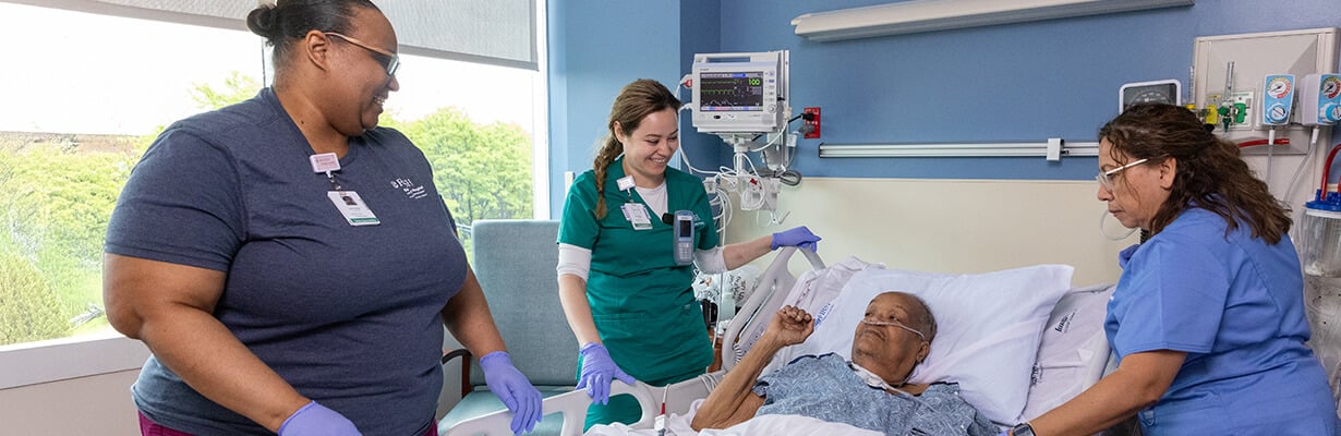 Woman laying in hospital bed, surrounded by nurses and physical therapists.