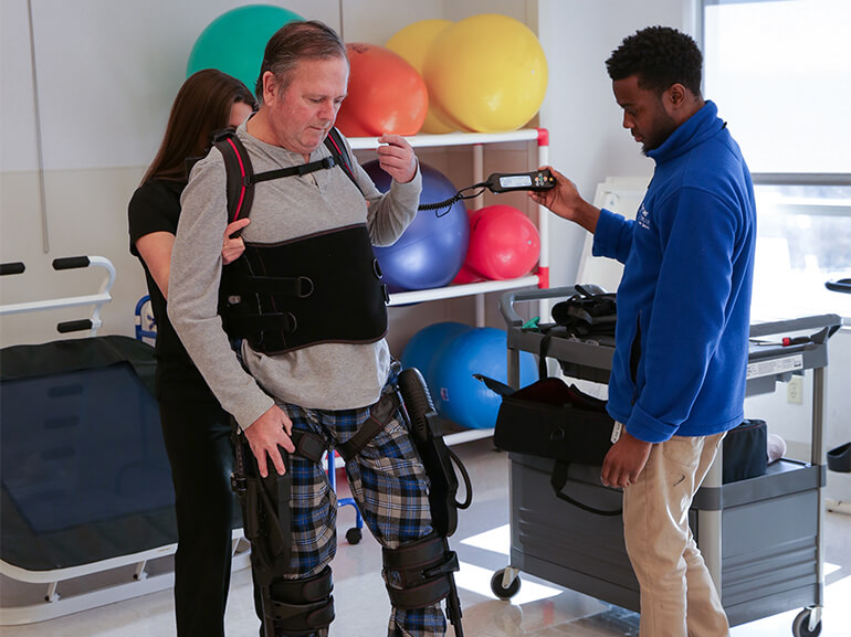 A male patient uses an robotic walking device to recover the ability to walk while being supported by his therapy team.